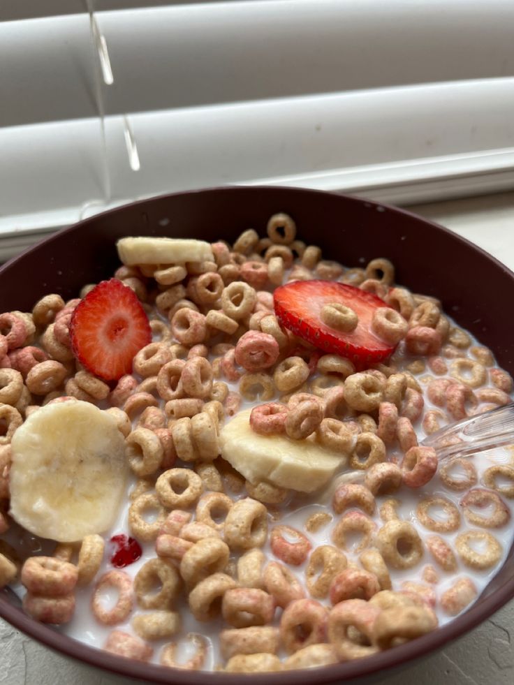 cereal with bananas, strawberries and milk in a bowl on a window sill