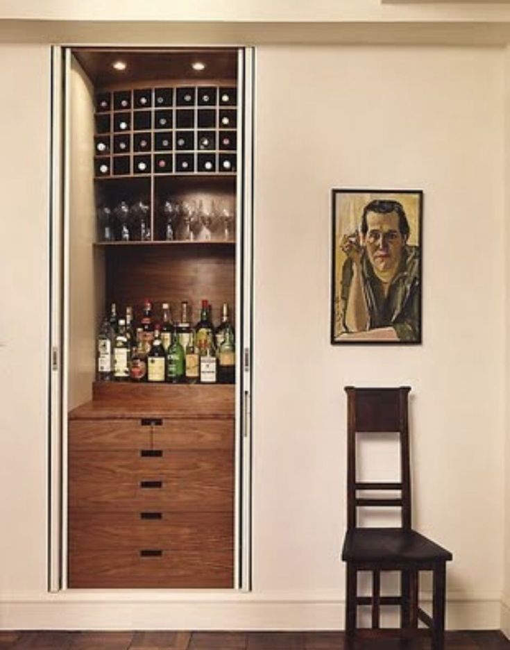 an empty chair sits in front of a cabinet with wine bottles on it and a painting hanging above