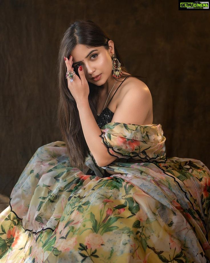 a woman sitting on top of a bed wearing a dress and holding her hand to her face