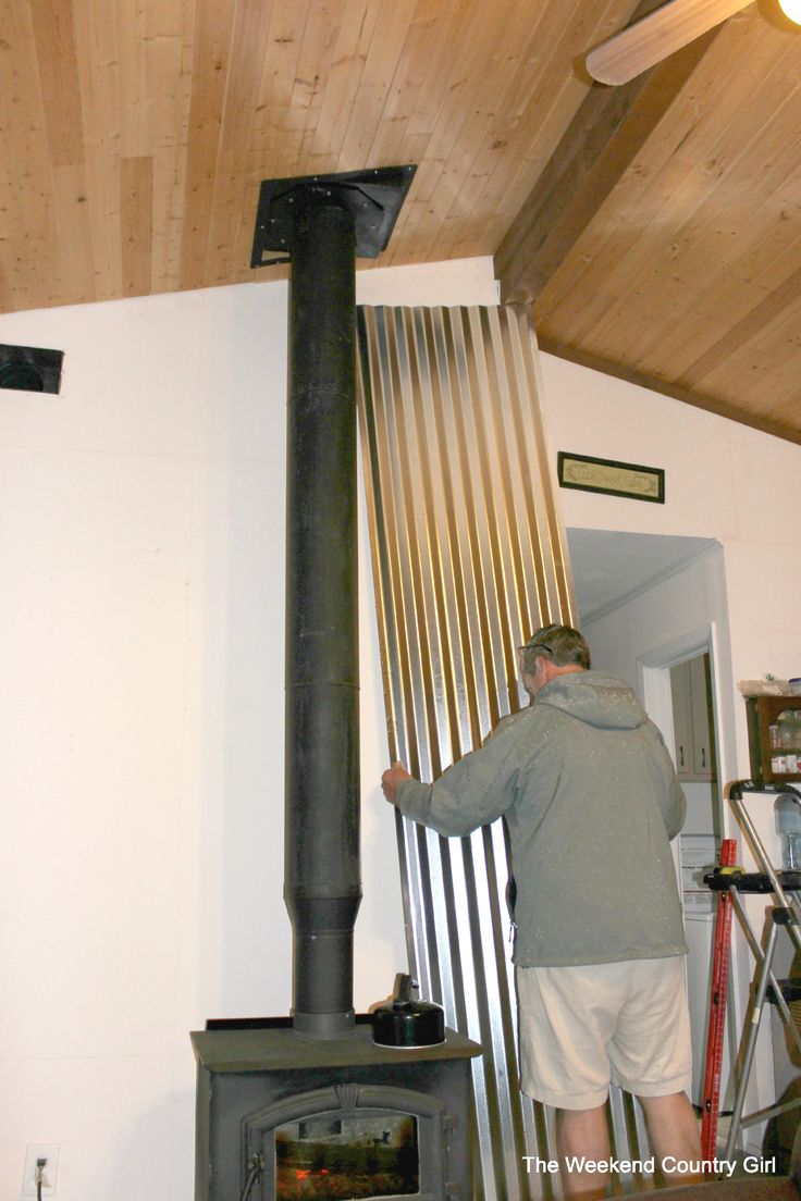 a man standing next to a wood stove in a living room under a wooden ceiling