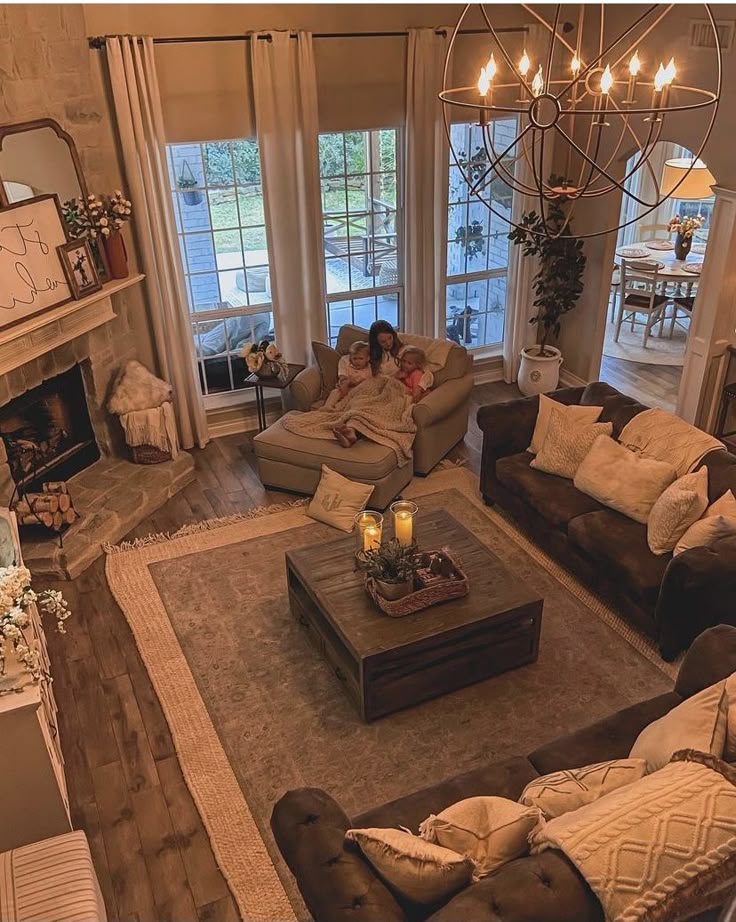 two people sitting on couches in a living room with fireplace and large windows overlooking the yard