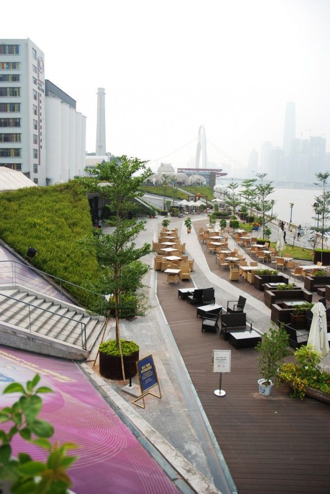 an outdoor seating area next to the water with benches and trees on each side in front of it