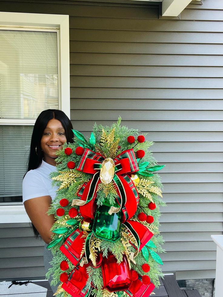 a woman standing in front of a house holding a christmas wreath