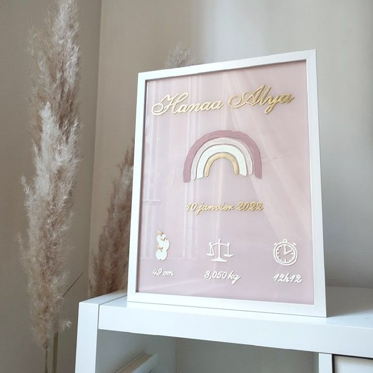 a white shelf with a pink and gold framed sign on it next to a plant