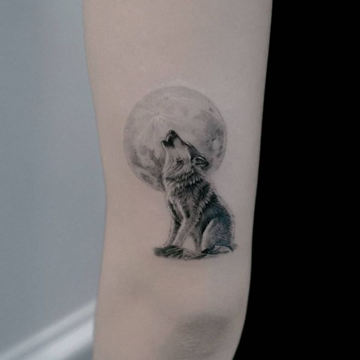 a small wolf tattoo on the right inner arm and lower arm, with a full moon in the background