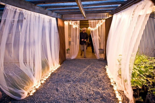 an outdoor area with white curtains and lights on the ceiling, surrounded by graveled ground