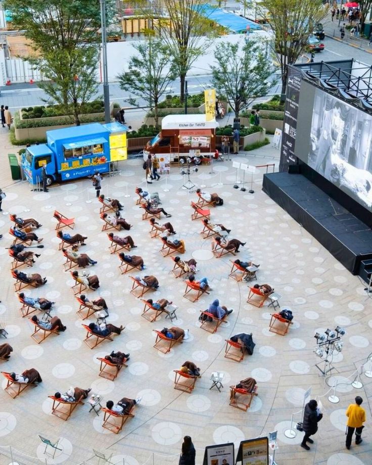 an aerial view of people sitting at tables in the middle of a courtyard with large screens