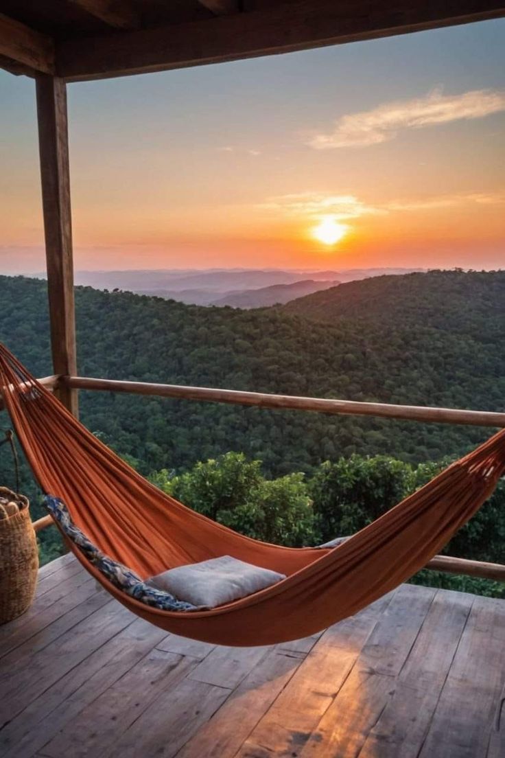 a hammock hanging from a porch with the sun setting in the sky behind it