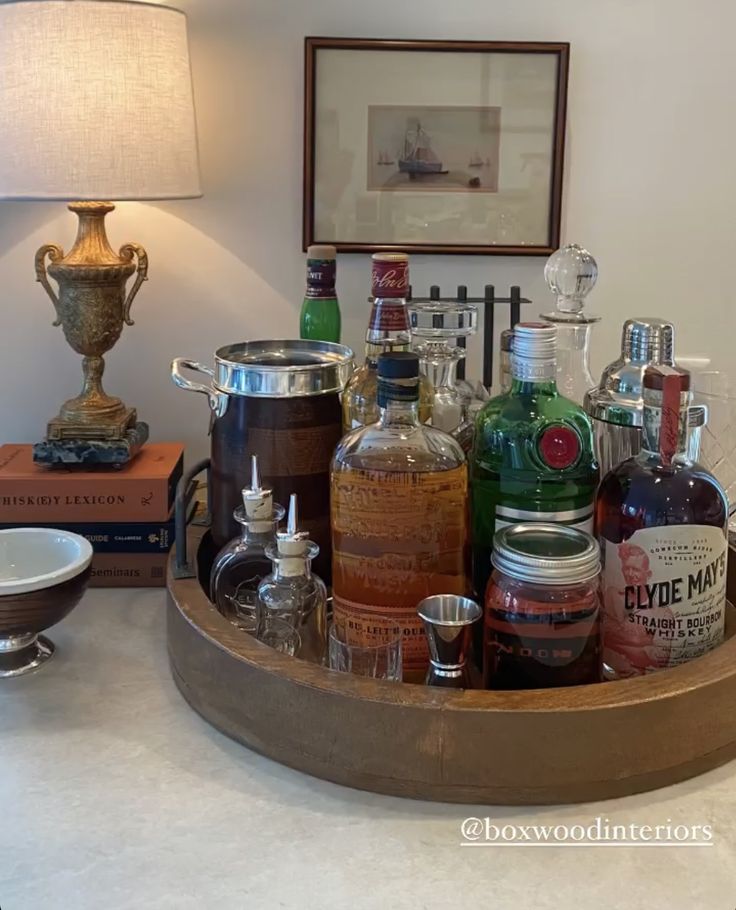 an assortment of liquor bottles on a tray in a living room with a table lamp