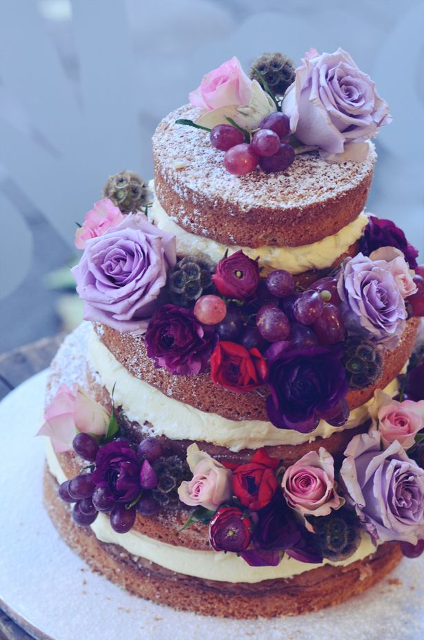 a multi layer cake with flowers and berries on the top is sitting on a plate