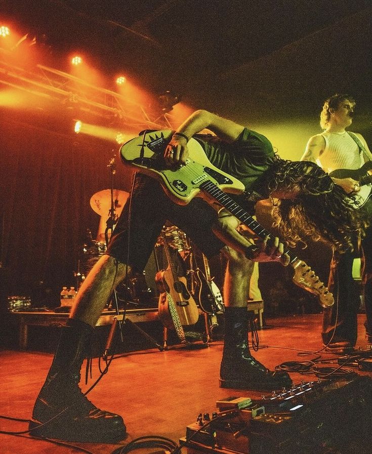 a man on stage with a guitar in his hand and another person standing behind him