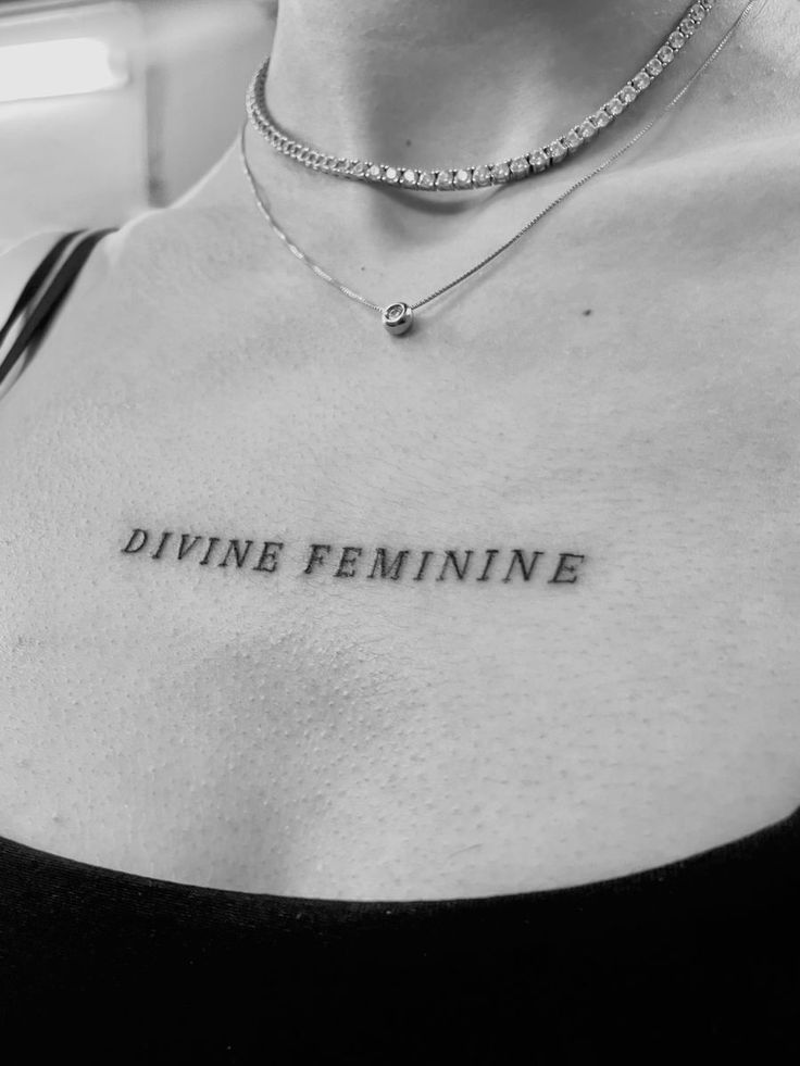 a woman with a tattoo on her chest that says divine feminine in cursive writing