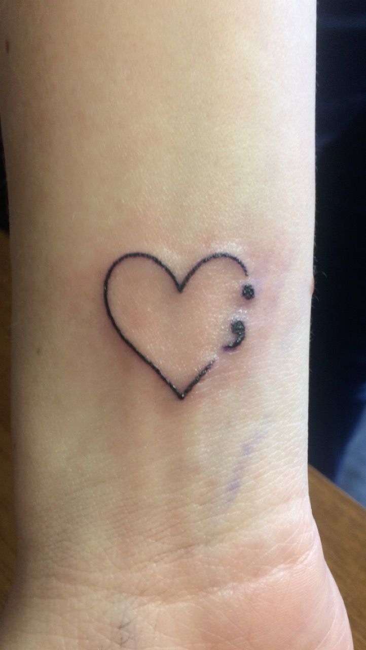 a small tattoo on the wrist of a woman with a heart shaped outline in black ink