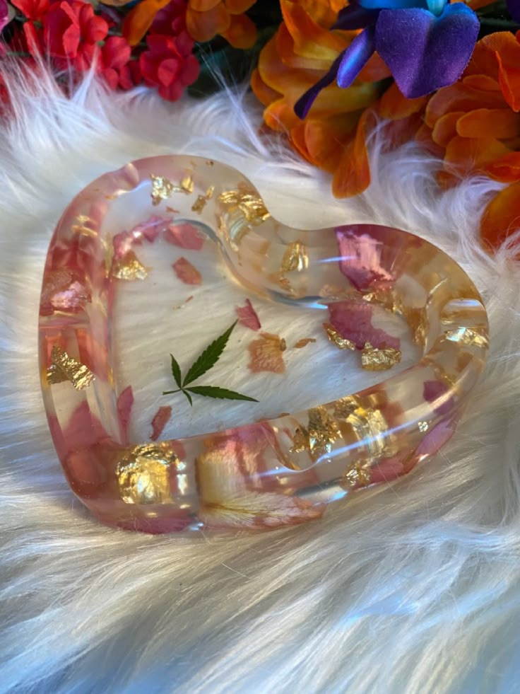 a pink heart shaped brooch sitting on top of a white fur covered floor next to flowers