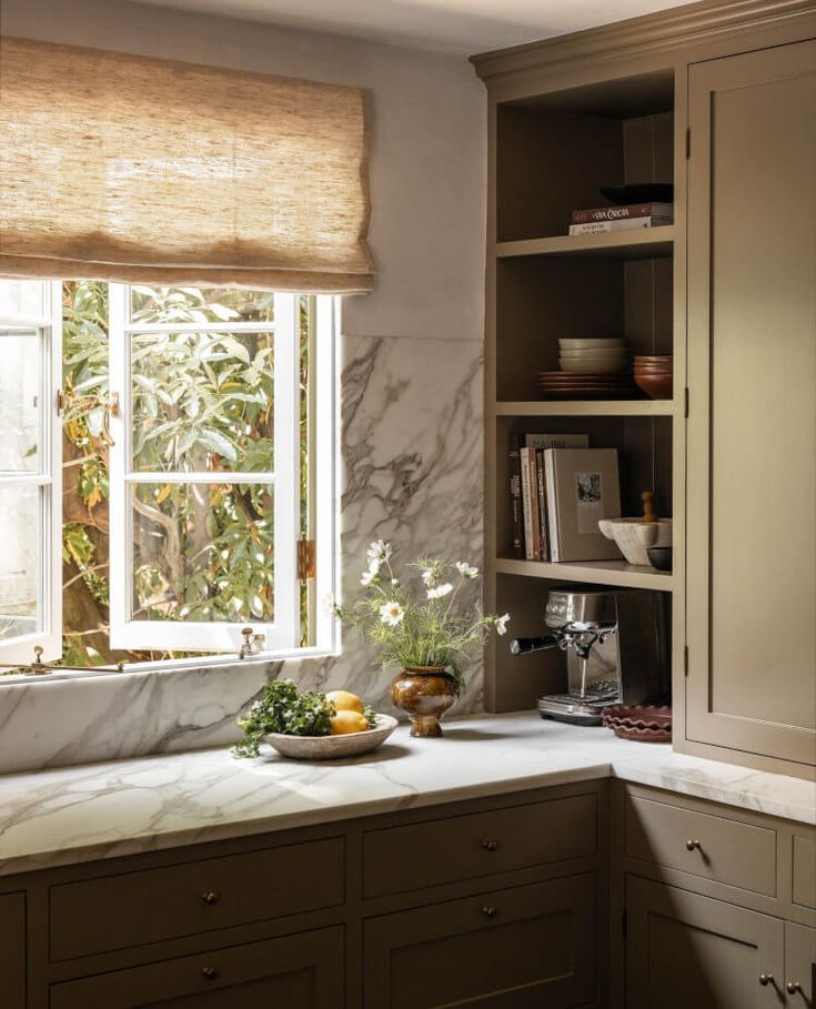 a kitchen with marble counter tops and wooden cabinets in front of a large open window