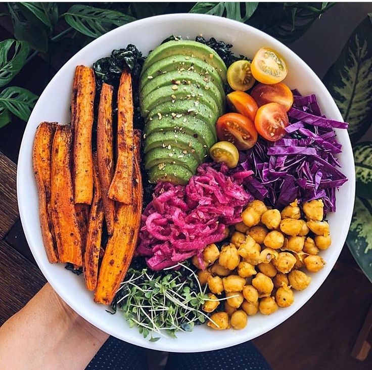 a white bowl filled with different types of food on top of a wooden table next to plants