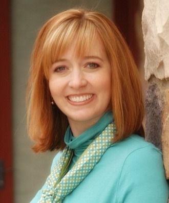 a woman with red hair wearing a blue jacket and green scarf standing next to a stone statue