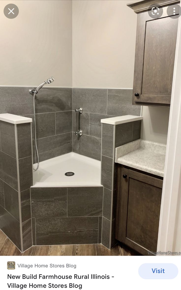 a bathroom with gray tile and wooden cabinets in it's corner shower stall area