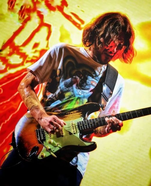 a man playing an electric guitar in front of a colorful wall with graffiti on it