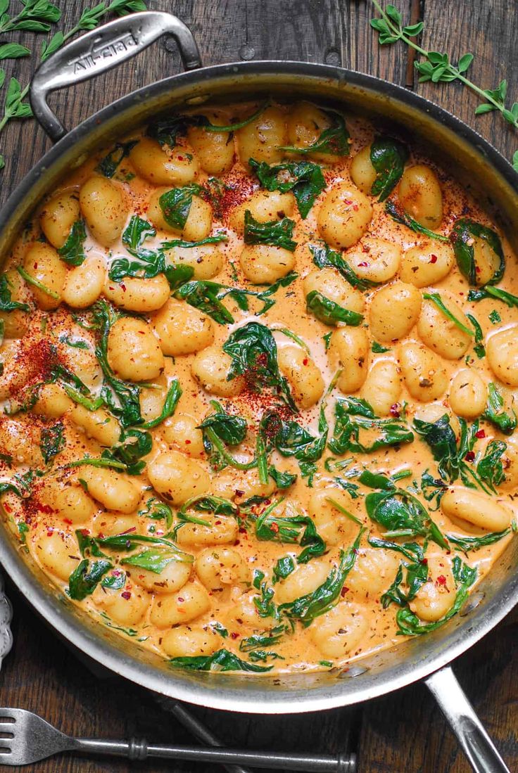 a pan filled with gnocchini and spinach on top of a wooden table