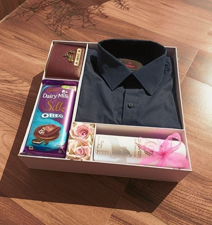 an open box with some items inside on a wooden floor next to a pink ribbon