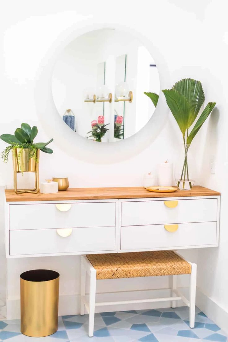 a white dresser with two drawers and a mirror on the wall next to potted plants