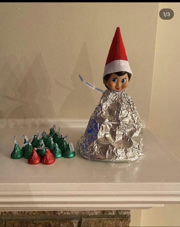 an elf doll sitting on top of a table next to some candy canes and wrapped in tin foil