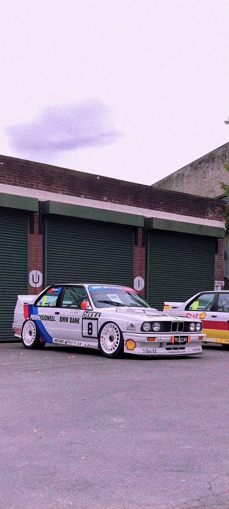 two bmws parked in front of a building with garage doors on the side and one is white