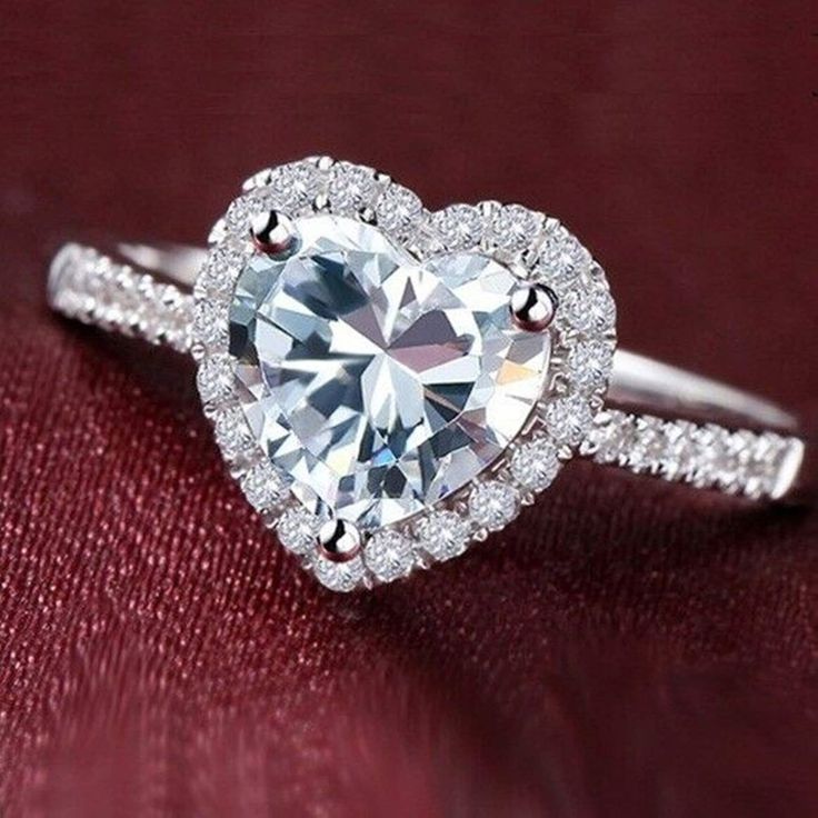 a heart shaped diamond ring on top of a red cloth