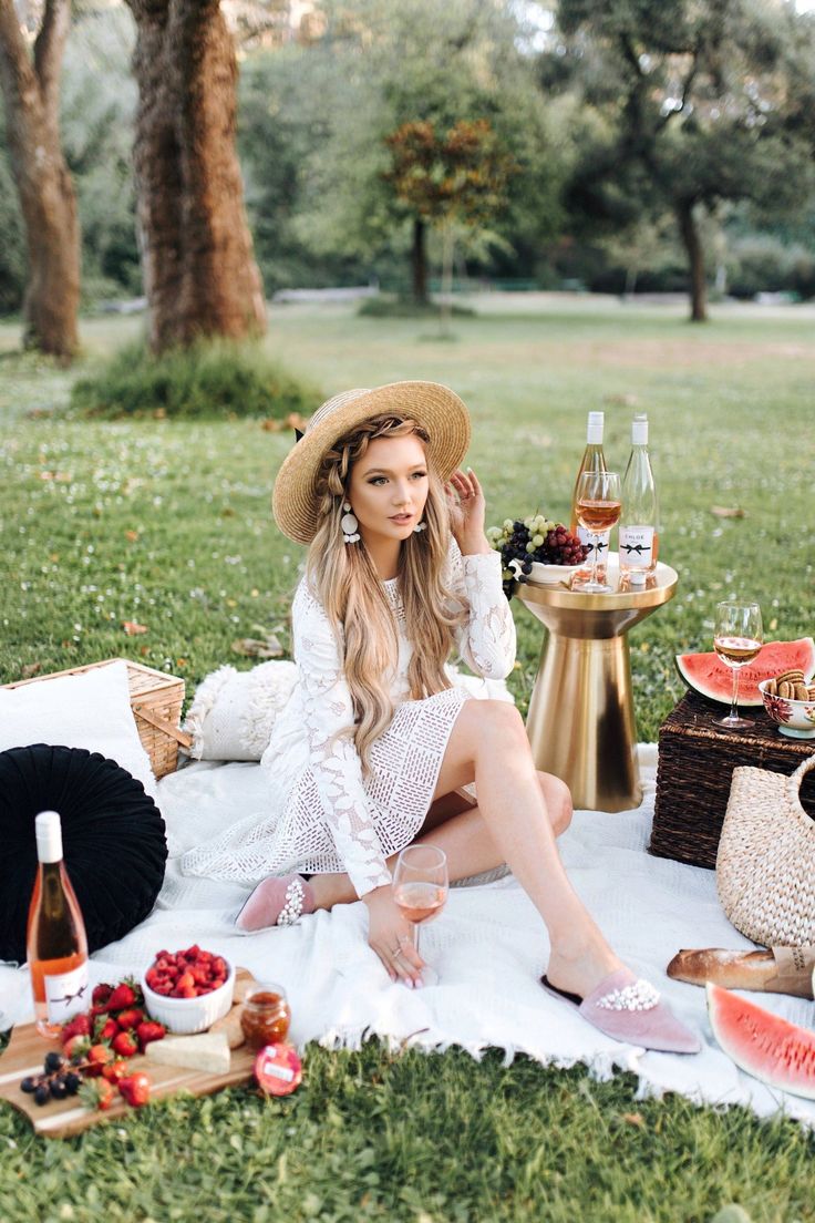 a woman sitting on top of a blanket next to a picnic table filled with food