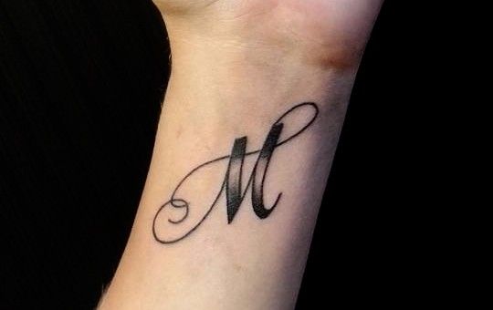 a wrist tattoo with the letter m on it