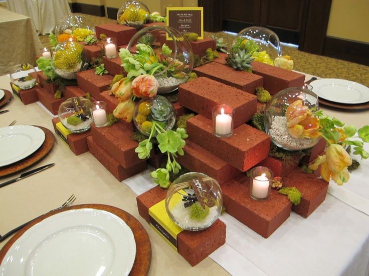 the table is set with candles, plates and flowers in vases on top of red bricks