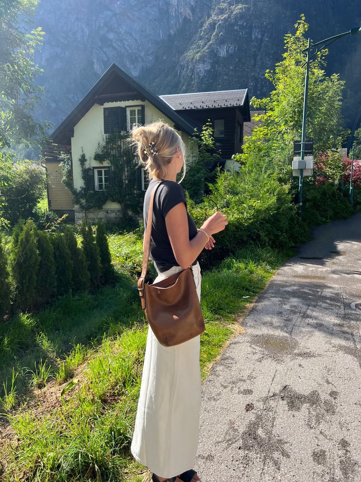 a woman standing on the side of a road holding a brown purse in her hand