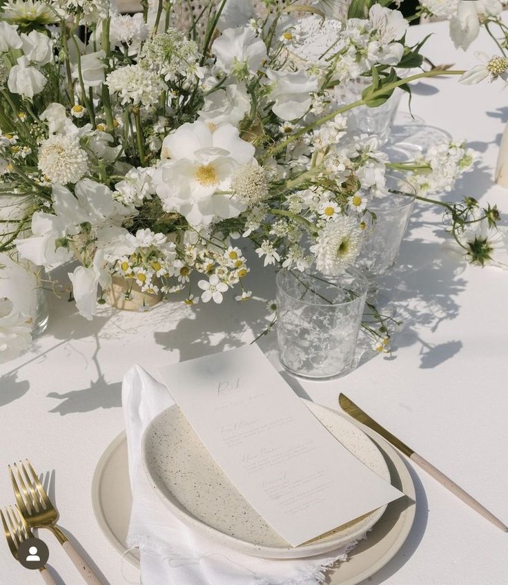 the table is set with white flowers and silverware