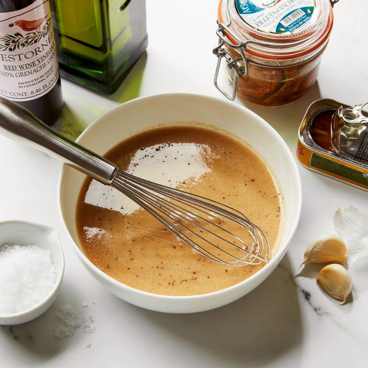 a bowl filled with liquid and whisk on top of a table next to other ingredients