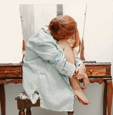 a woman sitting in front of a mirror on top of a wooden stool with her legs crossed