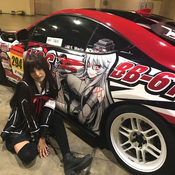 a woman sitting on the ground next to a car with anime characters painted on it