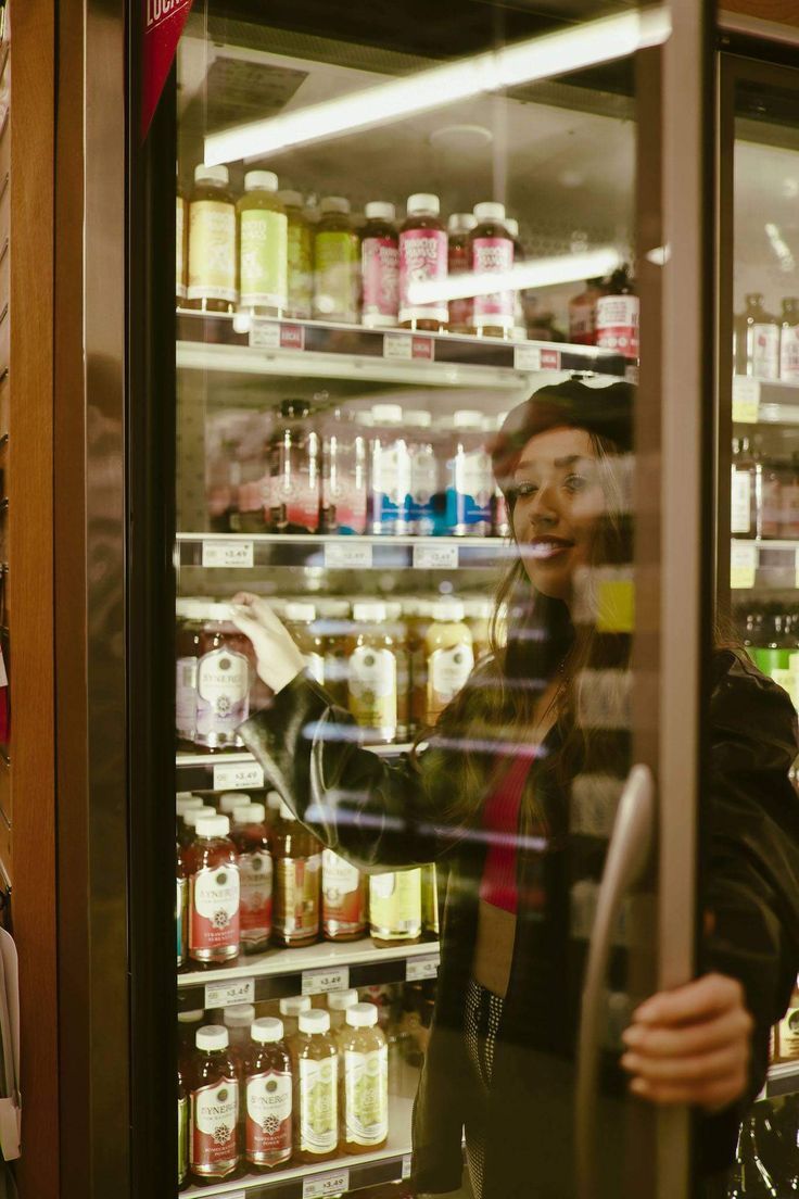 a woman standing in front of a display case filled with lots of food and drinks