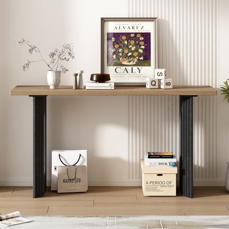 a wooden table topped with books next to a white vase filled with flowers on top of a hard wood floor