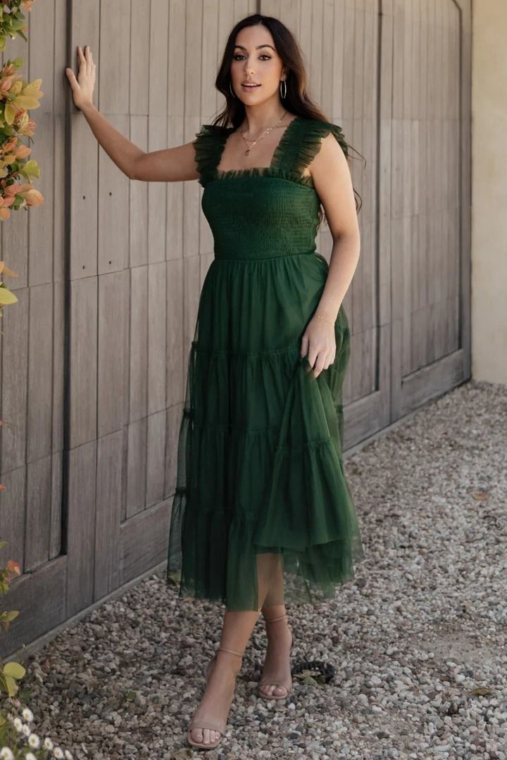 a woman in a green dress leaning against a wooden fence with her hand on the wall