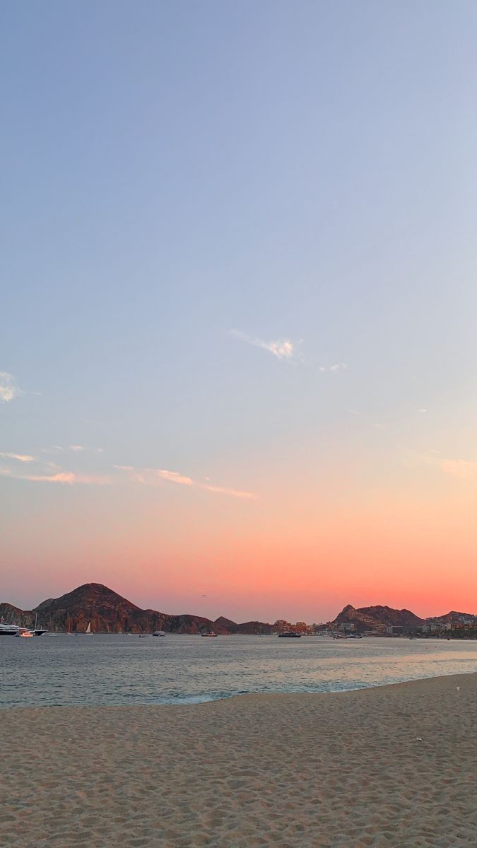 a person is flying a kite on the beach at sunset with mountains in the background