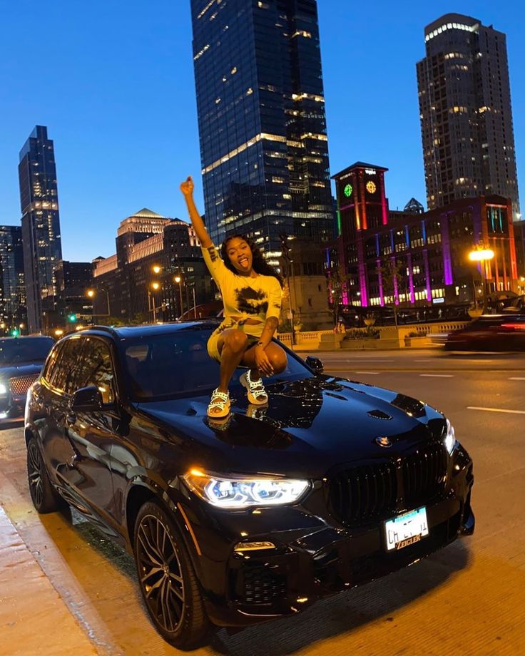 a person jumping on top of a black car in the middle of a city at night