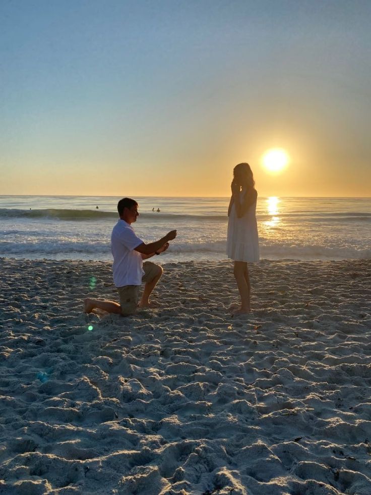 a man kneeling down next to a woman on top of a sandy beach