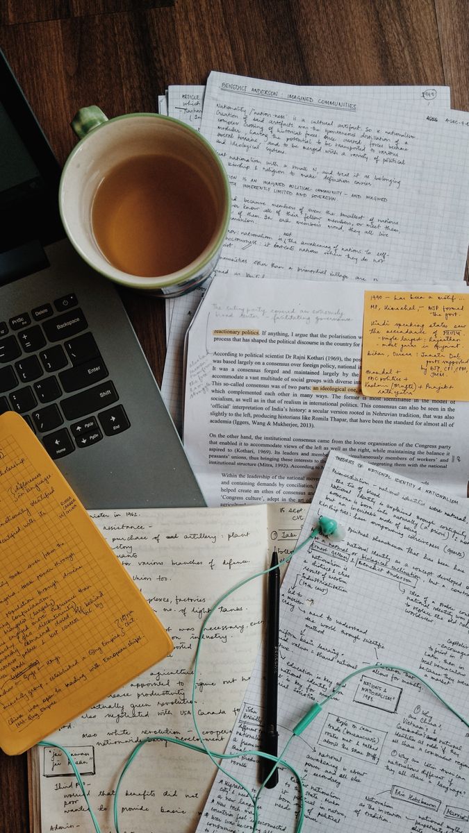 an open laptop computer sitting on top of a wooden table next to papers and a cup of coffee