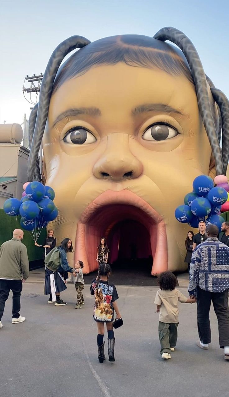 people standing in front of a giant head with blue balloons