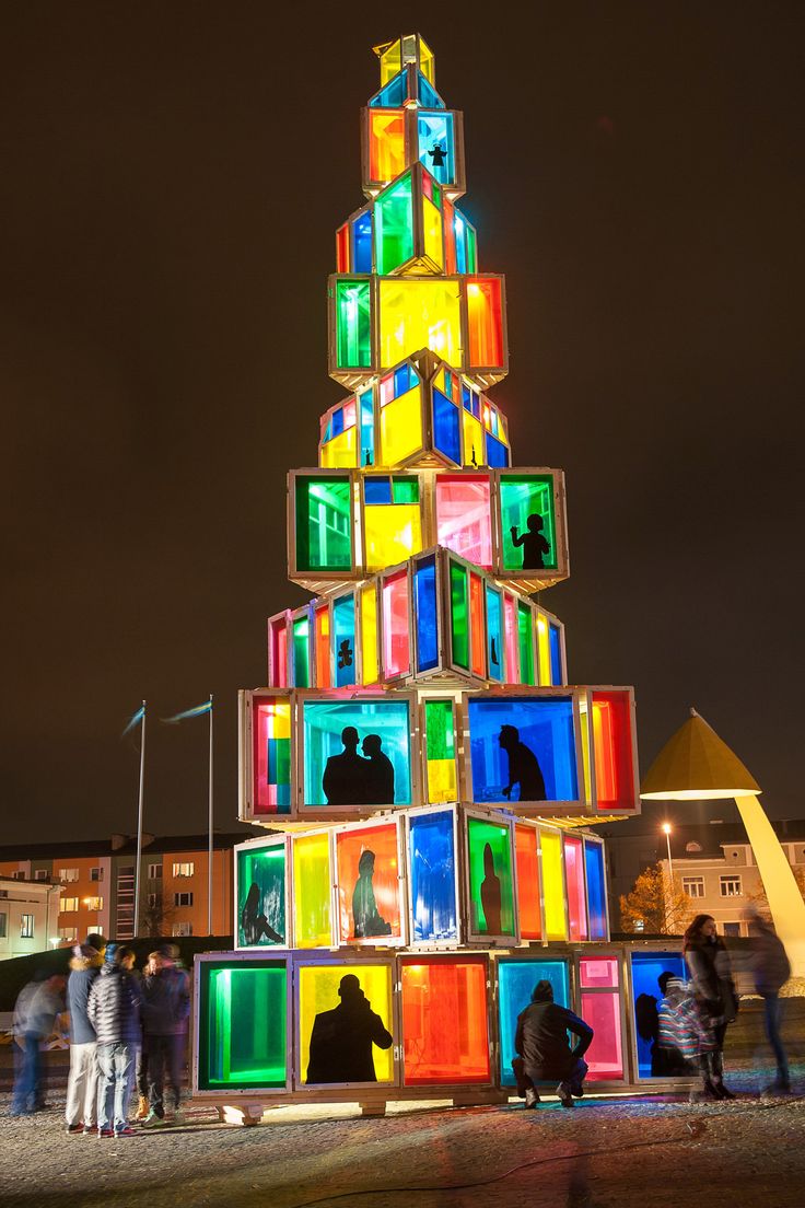 people standing in front of a multicolored christmas tree made out of cubes