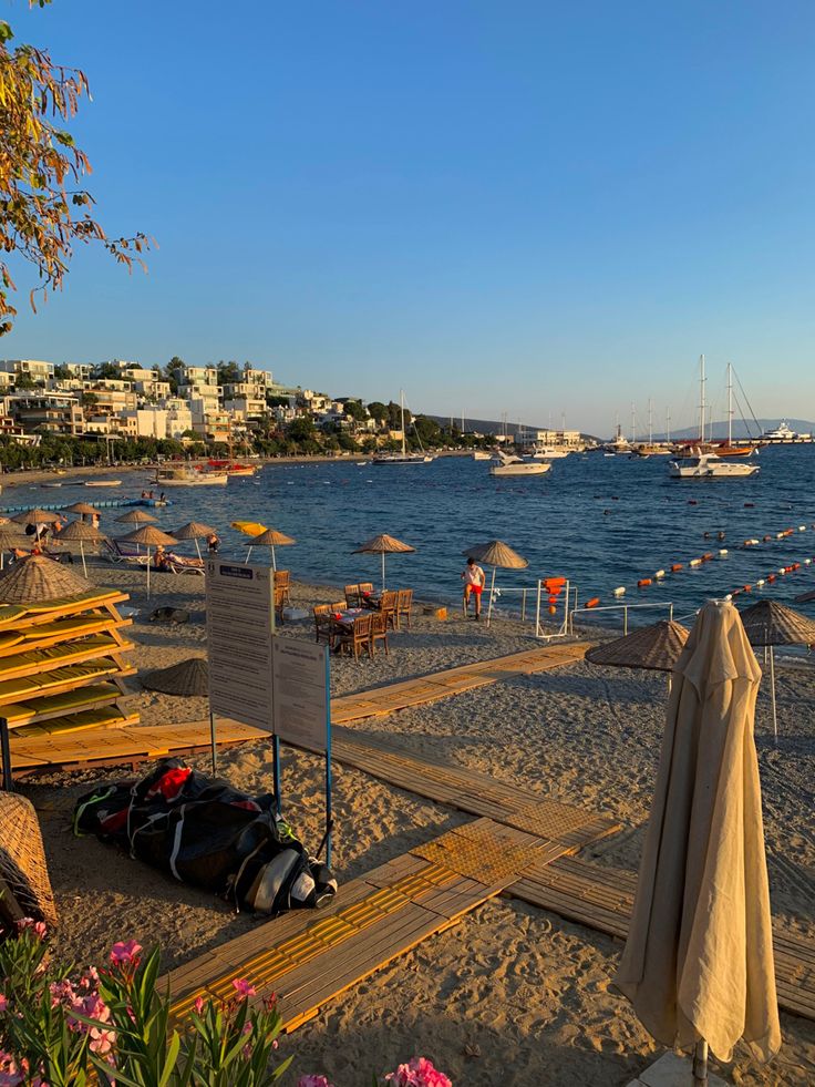 there are many umbrellas on the beach by the water and boats in the distance