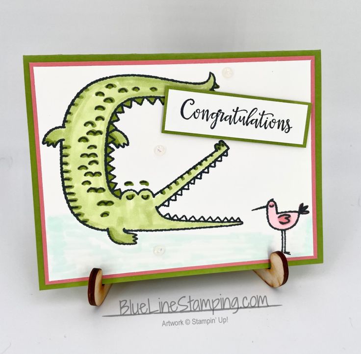 a handmade congratulations card with a green alligator holding a pink flamingo on it