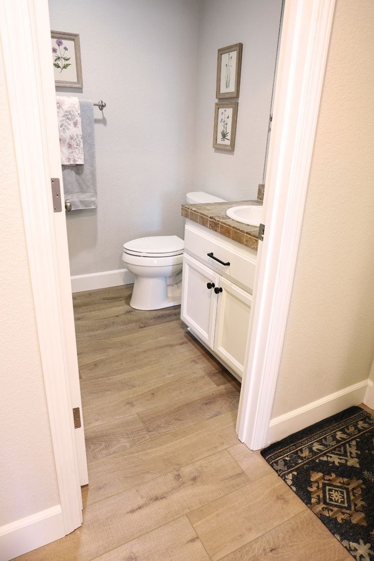 a white toilet sitting in a bathroom next to a sink under a mirror on top of a wooden floor