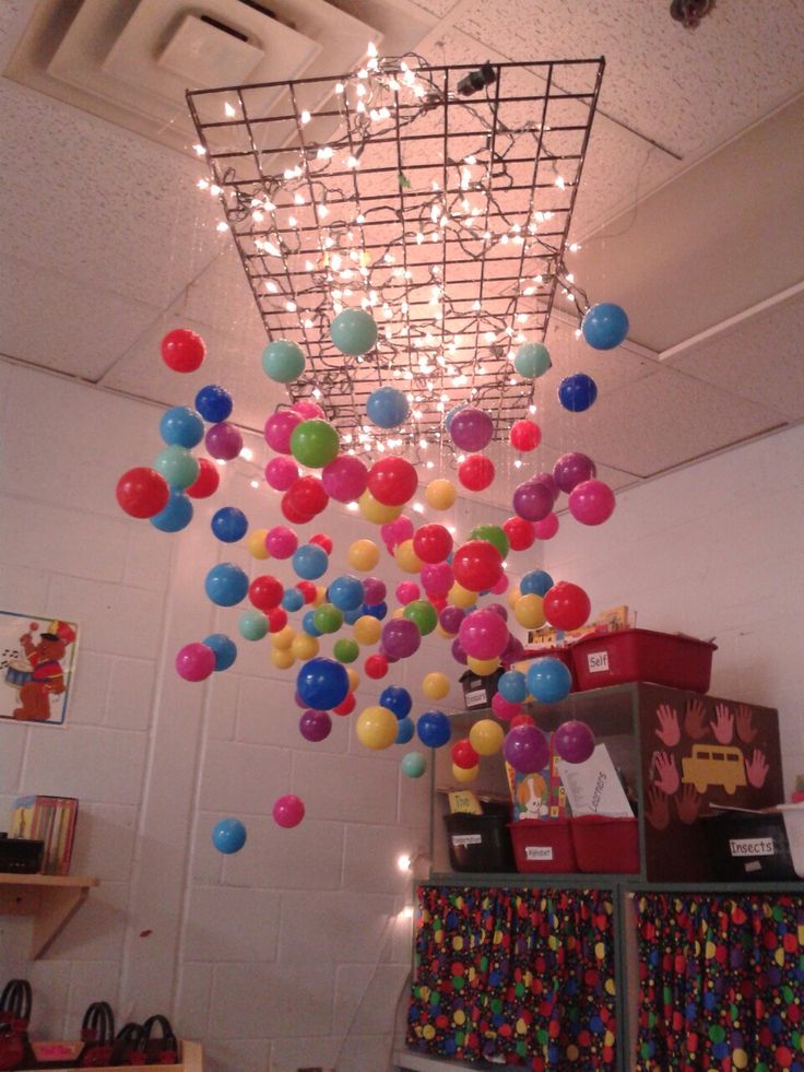 a room filled with lots of colorful balloons hanging from the ceiling and lights on the ceiling